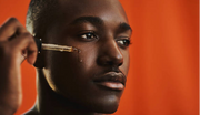 A male model posed with a dropper to apply serum on his face.