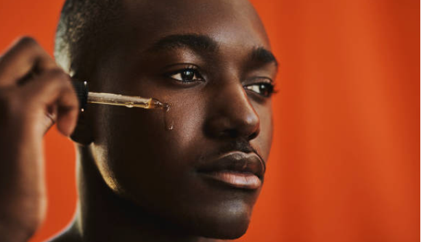 A male model posed with a dropper to apply serum on his face.